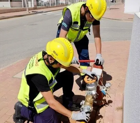 Dos operarios con casco y chaleco de seguridad revisando una boca de incendios en una zona urbana.